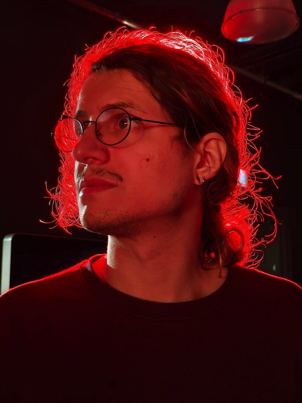 Portrait of João Lazaro, lit from behind by red light, looking to the side