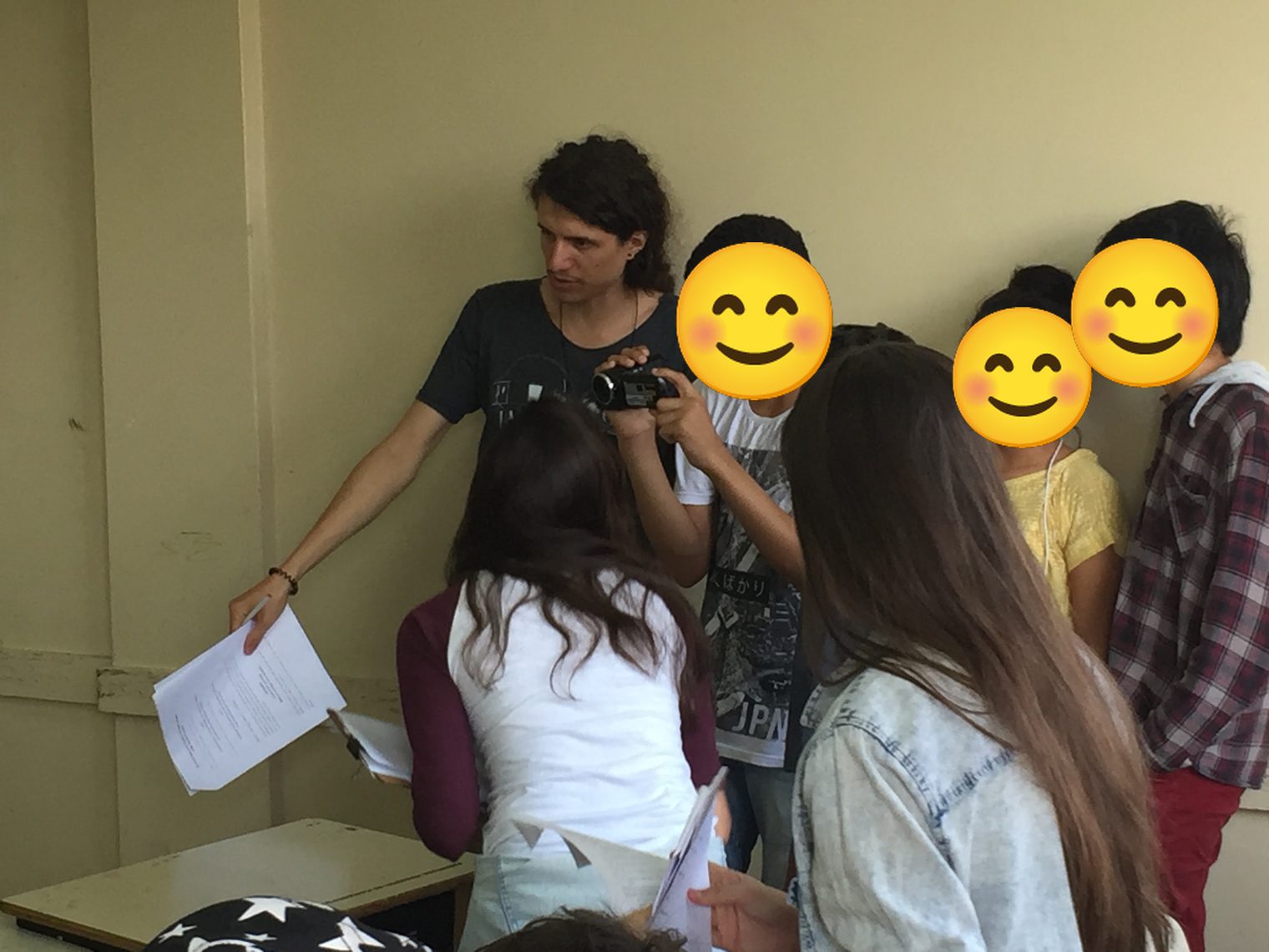 João Lazaro leading an Educom.cine workshop, handing out papers while a group of school students looks at a video camera; students' faces covered