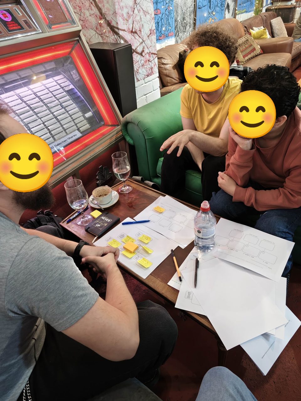 Three Newcastle Film Club members at a table during the Script Workshop, outlining a short film's scenes with yellow post-it notes on story-structure sheets; faces covered